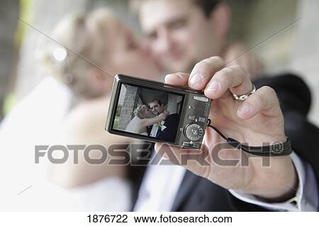 Ontario, Canada; A Groom Holds A Camera And Takes A Self-Portrait Of His Bride Kissing His Cheek View Large Photo Image Stock Image - Ontario, Canada; A Groom Holds A Camera And Takes A Self-Portrait Of His Bride Kissing His Cheek. Fotosearch