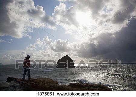 Pacific City, Oregon, United States Of America; A Man Standing On The Coast And Looking At Haystack Rock At Cape Kiwanda View Large Photo Image Stock Image - Pacific City, Oregon, United States Of America; A Man Standing On The Coast And Looking At Haystack Rock At Cape Kiwanda. Fotosearch