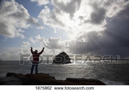 Pacific City, Oregon, United States Of America; Silhouette Of A Man With Arms Raised Looking At Haystack Rock At Cape Kiwanda View Large Photo Image Stock Image - Pacific City, Oregon, United States Of America; Silhouette Of A Man With Arms Raised Looking At Haystack Rock At Cape Kiwanda. Fotosearch