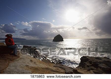 Pacific City, Oregon, United States Of America; A Man Sitting On The Coast With A View Of Haystack Rock At Cape Kiwanda View Large Photo Image Stock Image - Pacific City, Oregon, United States Of America; A Man Sitting On The Coast With A View Of Haystack Rock At Cape Kiwanda. Fotosearch
