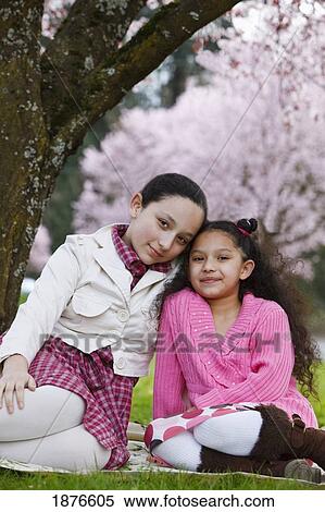 Stock Photography - Portland, Oregon, United States Of America; Two Sisters Sitting Under A Cherry Blossom Tree In Spring In Westmorland Park. Fotosearch