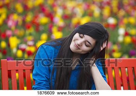 Stock Photo - Woodburn, Oregon, United States Of America; A Teenage Girl Sits On A Red Bench In Front Of A Tulip Field At Wooden Shoe Tulip Farm. Fotosearch