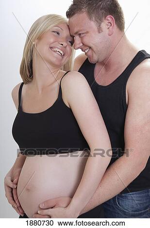 Stock Image - a man embracing a pregnant woman as they touch her bare belly. Fotosearch