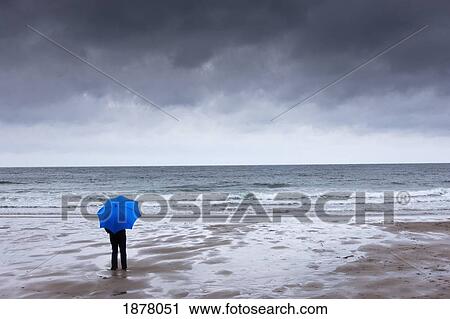 a person holding a blue umbrella standing on the beach with a dark sky overhead; newton, northumberland, england View Large Photo Image Stock Image - a person holding a blue umbrella standing on the beach with a dark sky overhead; newton, northumberland, england. Fotosearch
