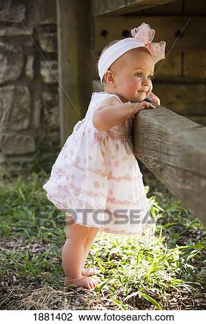 Stock Image - baby girl standing against a fence; nashville, tennessee, united states of america. Fotosearch