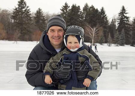 Stock Photograph - edmonton, alberta, canada; a father and son on an outdoor ice rink. Fotosearch