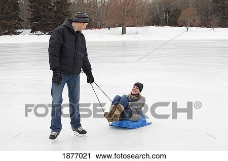 edmonton, alberta, canada; a man pulling a woman on a small sled across the ice on an outdoor rink View Large Photo Image Stock Image - edmonton, alberta, canada; a man pulling a woman on a small sled across the ice on an outdoor rink. Fotosearch