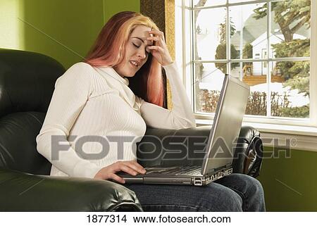 edmonton, alberta, canada; a woman looking frustrated as she works on her laptop computer while sitting in a comfortable chair View Large Photo Image Picture - edmonton, alberta, canada; a woman looking frustrated as she works on her laptop computer while sitting in a comfortable chair. Fotosearch