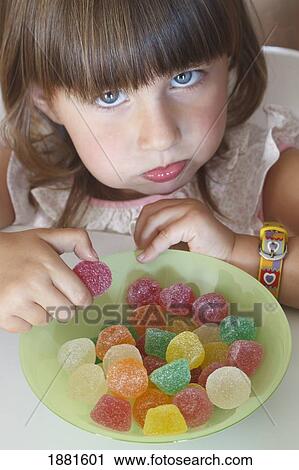 Stock Image - greedy looking two year old girl eating from a bowl of candies. Fotosearch