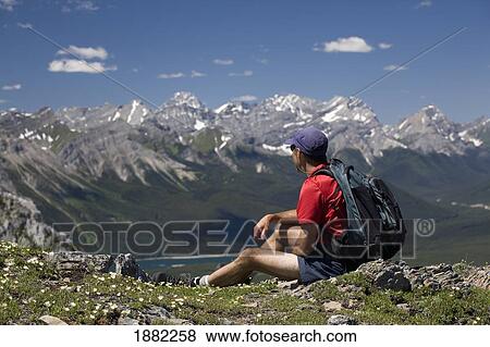 male hiker sitting on top of a ridge overlooking a mountain valley and lake; alberta, canada View Large Photo Image Stock Photo - male hiker sitting on top of a ridge overlooking a mountain valley and lake; alberta, canada. Fotosearch