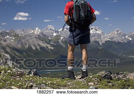 Stock Photo - male hiker standing on top of a ridge overlooking a mountain valley and lake; alberta, canada. Fotosearch