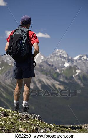 Stock Photo - male hiker standing on top of a ridge overlooking a mountain valley; alberta, canada. Fotosearch