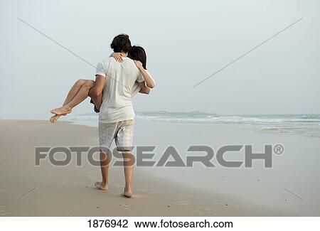 Stock Image - tarifa, cadiz, andalusia, spain; a man carrying a woman down los lances beach in costa de la luz. Fotosearch