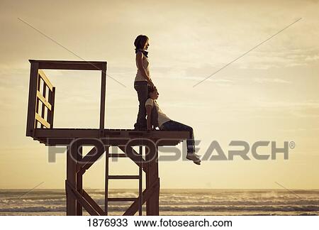 Stock Image - tarifa, cadiz, andalusia, spain; a mother and daughter on a wooden tower on los lances beach at sunset along costa de la luz. Fotosearch