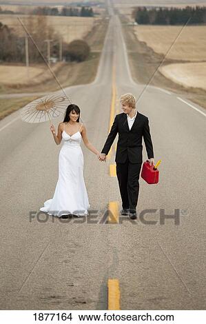 three hills, alberta, canada; a bride and groom walking down a rural road holding a jerry can and a parasol View Large Photo Image Picture - three hills, alberta, canada; a bride and groom walking down a rural road holding a jerry can and a parasol. Fotosearch