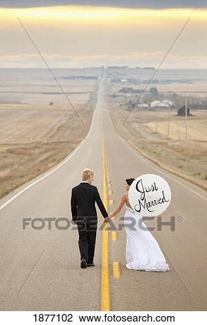 three hills, alberta, canada; a bride and groom walking down a rural road with the bride holding a parasol with 'just married' written on it View Large Photo Image Stock Image - three hills, alberta, canada; a bride and groom walking down a rural road with the bride holding a parasol with 'just married' written on it. Fotosearch