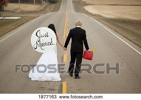 three hills, alberta, canada; a bride and groom walking down a rural road holding a jerry can and a parasol saying 'just married' View Large Photo Image Stock Image - three hills, alberta, canada; a bride and groom walking down a rural road holding a jerry can and a parasol saying 'just married'. Fotosearch