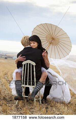 three hills, alberta, canada; a bride and groom sitting on a chair in a farm field View Large Photo Image Stock Photo - three hills, alberta, canada; a bride and groom sitting on a chair in a farm field. Fotosearch