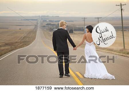 Stock Photo - three hills, alberta, canada; a bride and groom on a rural road with the bride holding a parasol with the words 'just married' written on it. Fotosearch