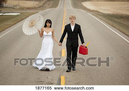 Stock Photography - three hills, alberta, canada; a bride and groom walking down a rural road holding a jerry can and a parasol. Fotosearch