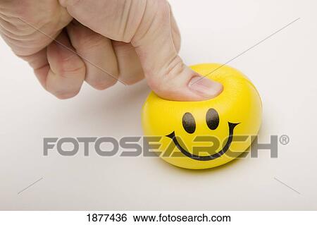 Stock Photograph - yellow happy face being squeezed by a thumb; edmonton, alberta, canada. Fotosearch