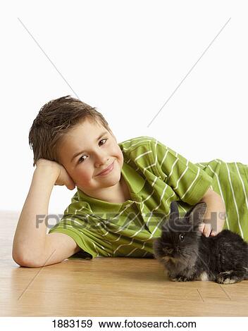 Stock Photo - A Boy Laying On The Floor Petting A Rabbit. Fotosearch