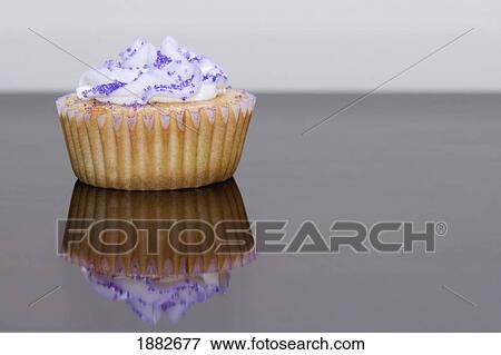 Stock Photo - A Cupcake Decorated With White Icing And Purple Sprinkles. Fotosearch