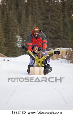 Stock Image - A Family Playing With A Toboggan In The Snow; Lake Louise, Alberta, Canada. Fotosearch