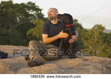Stock Photo - A Man Sits On A Rock With His Dog; Manica, Mozambique, Africa. Fotosearch