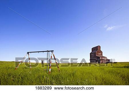 Stock Photo - A Man Walking Through A Field With An Old Swing Set And An Old Grain Elevator; Bents, Saskatchewan, Canada. Fotosearch
