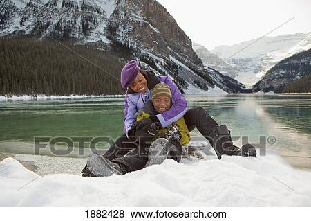 Stock Photo - A Mother With Her Son Sitting In The Snow; Lake Louise, Alberta, Canada. Fotosearch