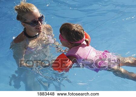 A Young Girl Wearing A Personal Floatation Device Vest And Armbands To Practice Swimming In A Pool With Her Mother View Large Photo Image Stock Photo - A Young Girl Wearing A Personal Floatation Device Vest And Armbands To Practice Swimming In A Pool With Her Mother. Fotosearch