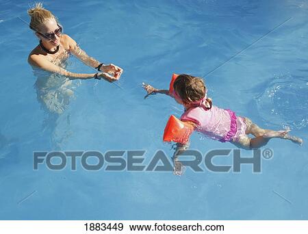 A Young Girl Wearing A Personal Floatation Device Vest And Armbands To Practice Swimming In A Pool With Her Mother View Large Photo Image Stock Photo - A Young Girl Wearing A Personal Floatation Device Vest And Armbands To Practice Swimming In A Pool With Her Mother. Fotosearch