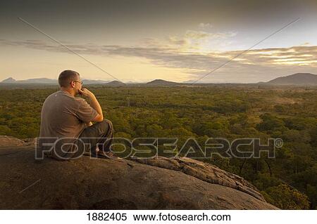 A Young Man Sitting On A Rock And Looking At The Landscape; Manica, Mozambique, Africa View Large Photo Image Stock Photography - A Young Man Sitting On A Rock And Looking At The Landscape; Manica, Mozambique, Africa. Fotosearch