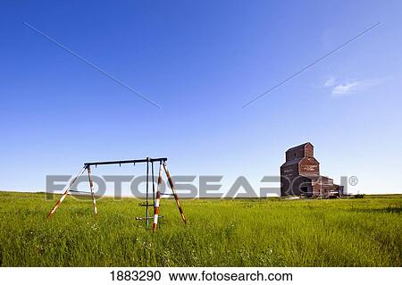 Stock Image - An Old Swing Set With A Grain Elevator Behind It In A Ghost Town; Bents, Saskatchewan, Canada. Fotosearch