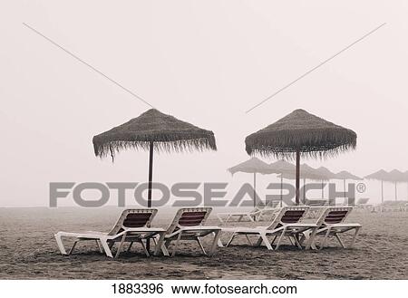 Stock Photograph - Sunbeds And Umbrella On Playamar Beach In Off-Season On A Foggy Day; Torremolinos, Malaga, Costa Del Sol, Spain. Fotosearch