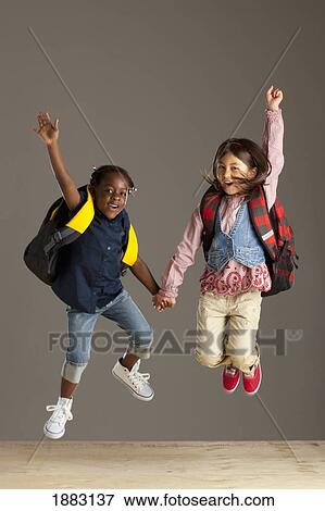 Stock Photo - Two Girls With Backpacks Holding Hands And Jumping Into The Air. Fotosearch