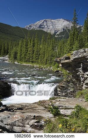 Stock Photograph - Waterfalls With Rock Ledge And Mountain In The Background; Alberta, Canada. Fotosearch