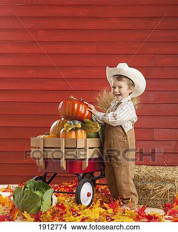 Picture - a boy dressed as a farmer with a wagon full of produce; three hills, alberta, canada. Fotosearch