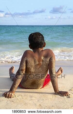 a boy sitting on the beach covered with sand and looking out at the water; maui, hawaii, united states of america View Large Photo Image Stock Image - a boy sitting on the beach covered with sand and looking out at the water; maui, hawaii, united states of america. Fotosearch
