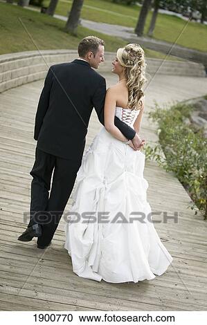 a bride and groom holding hands as they walk down a boardwalk on their wedding day; st. albert, alberta, canada View Large Photo Image Stock Image - a bride and groom holding hands as they walk down a boardwalk on their wedding day; st. albert, alberta, canada. Fotosearch