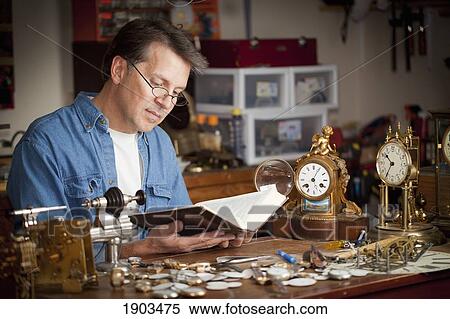 Stock Photography - a clock maker and repairman taking time to read his bible in his shop; st. catharines, ontario, canada. Fotosearch