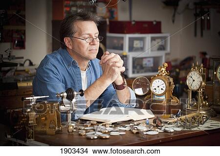 Picture - a clock maker prays at his desk in his shop; st. catharines, ontario, canada. Fotosearch