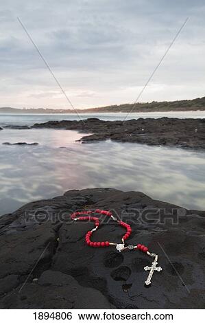Stock Photograph - a cross and rosary beads laying on a rock at flat rock; ballina, new south wales, australia. Fotosearch