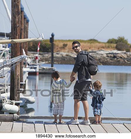 Stock Image - a father with his two sons on a pier looking at the boats; victoria, british columbia, canada. Fotosearch