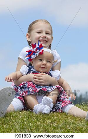 Stock Image - a girl holding her baby sister on the grass; portland, oregon, united states of america. Fotosearch