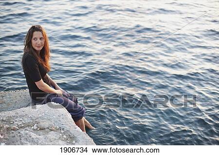 a girl sitting on a rock and dipping her feet into the water; hvar, croatia View Large Photo Image Picture - a girl sitting on a rock and dipping her feet into the water; hvar, croatia. Fotosearch