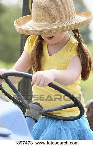 Stock Image - a girl with a straw hat with hands on the steering wheel of a tractor; troutdale, oregon, united states of america. Fotosearch