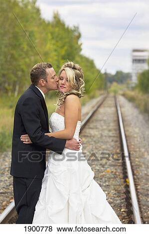 Stock Photo - a groom kisses his bride as they stand on railway tracks with an old grain elevator off in the distance; st. albert, alberta, canada. Fotosearch