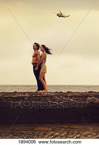 a man and woman standing in an embrace along the water in parque natural del estrecho at sunset with a helicopter in the sky overhead; tarifa, cadiz, andalusia, spain View Large Photo Image Stock Photograph - a man and woman standing in an embrace along the water in parque natural del estrecho at sunset with a helicopter in the sky overhead; tarifa, cadiz, andalusia, spain. Fotosearch